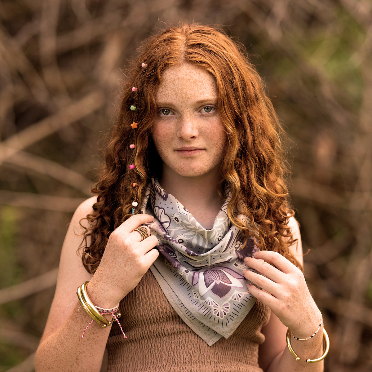 Young woman with curly red hair and a decorative scarf, standing outdoors