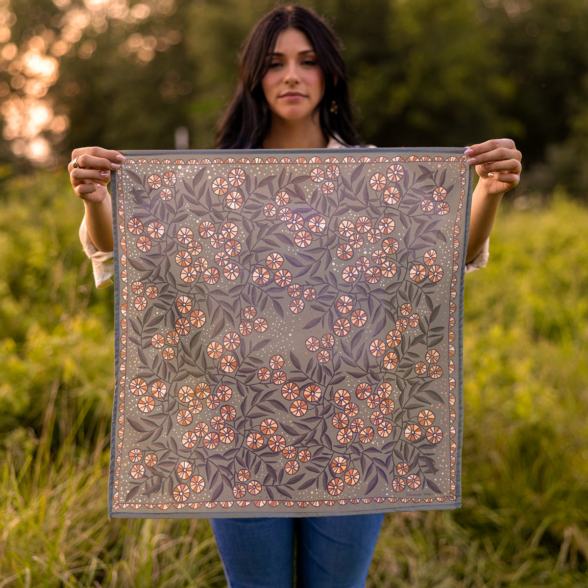 Front view of No. 114 Eleanor bandana held flat, warm-gray ground with peach floral clusters and leafy print outdoors