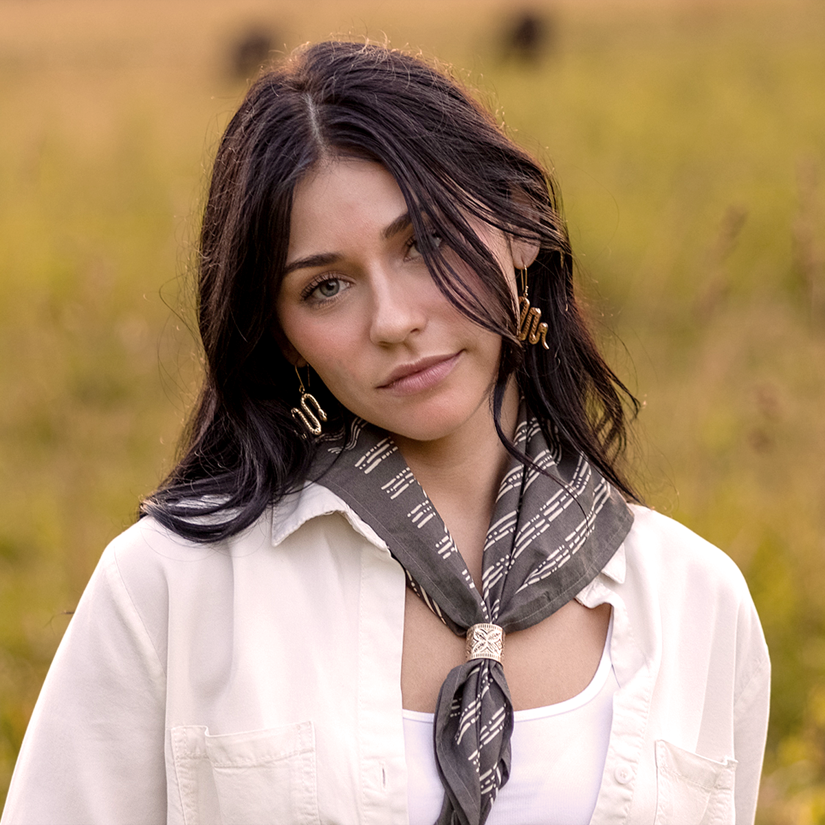 Person with dark hair wearing a scarf and white top in a field