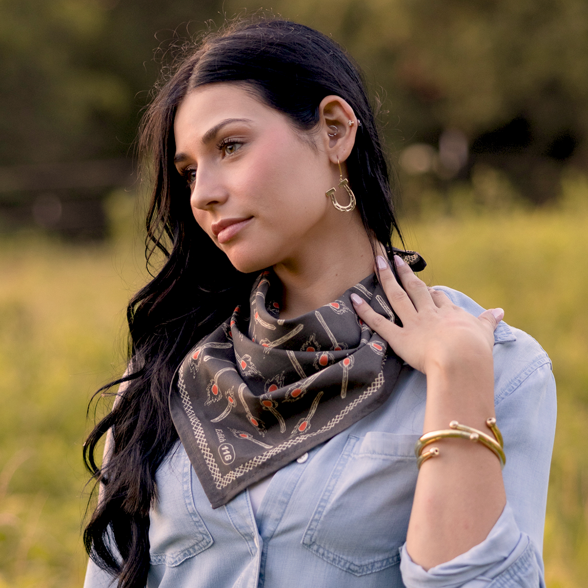 Angled view of No. 116 Edith bandana worn at the neck, charcoal gray with brown, orange and cream motifs, field background