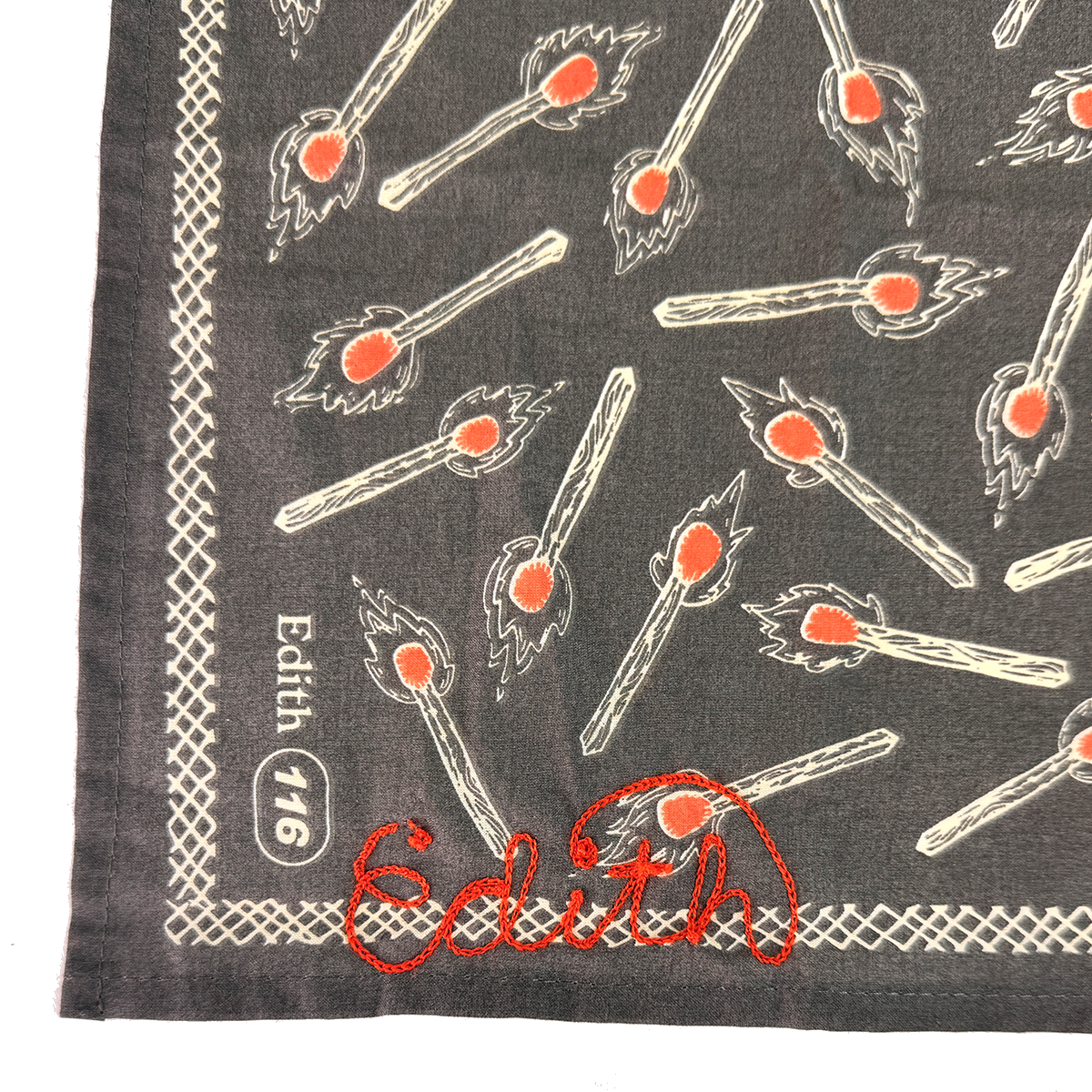 Close-up of No. 116 Edith bandana showing matchstick print and red chainstitch Edith signature on charcoal gray fabric, on white background