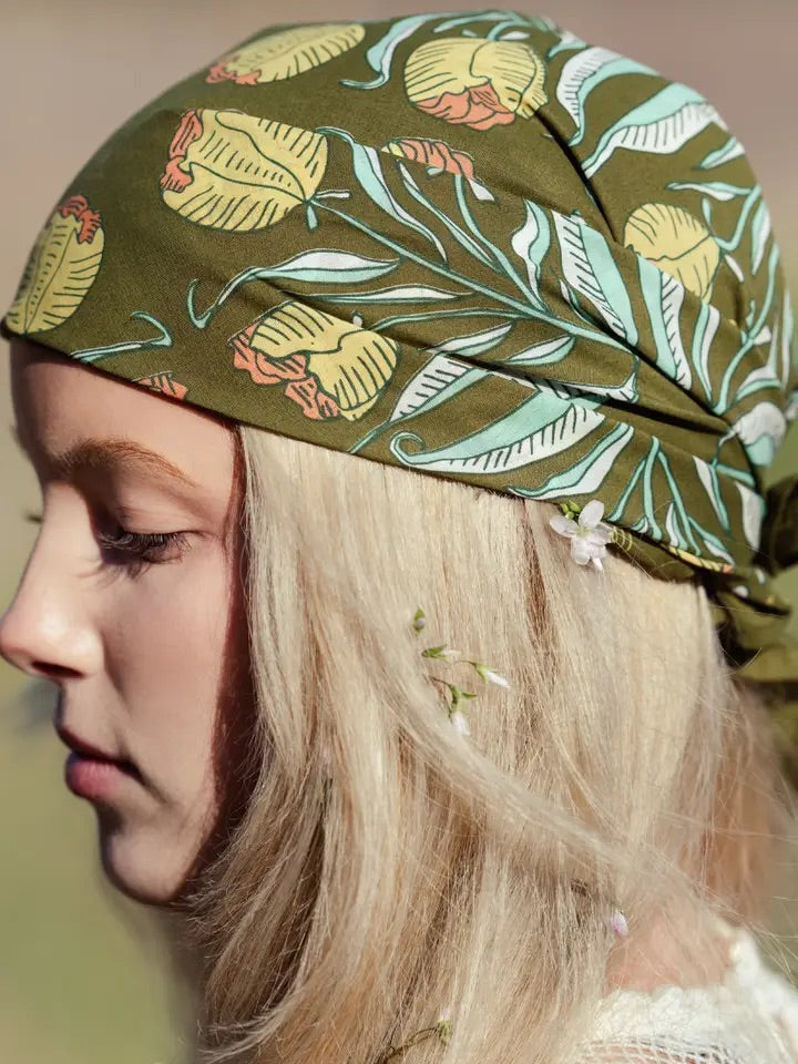 Model in profile wearing an olive green Adele bandana tied at the back showing mustard, brick, aqua, and cream floral print