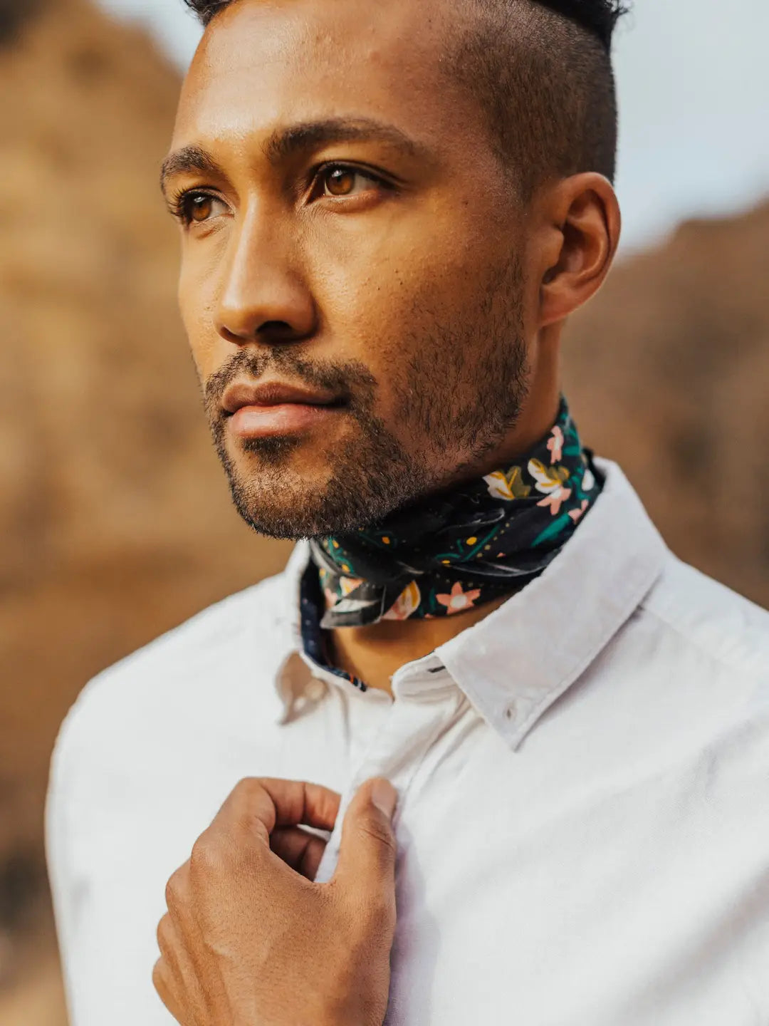 Close-up of Betty bandana tied at the neck showing black fabric with gold, pink and green floral print, worn with a white shirt