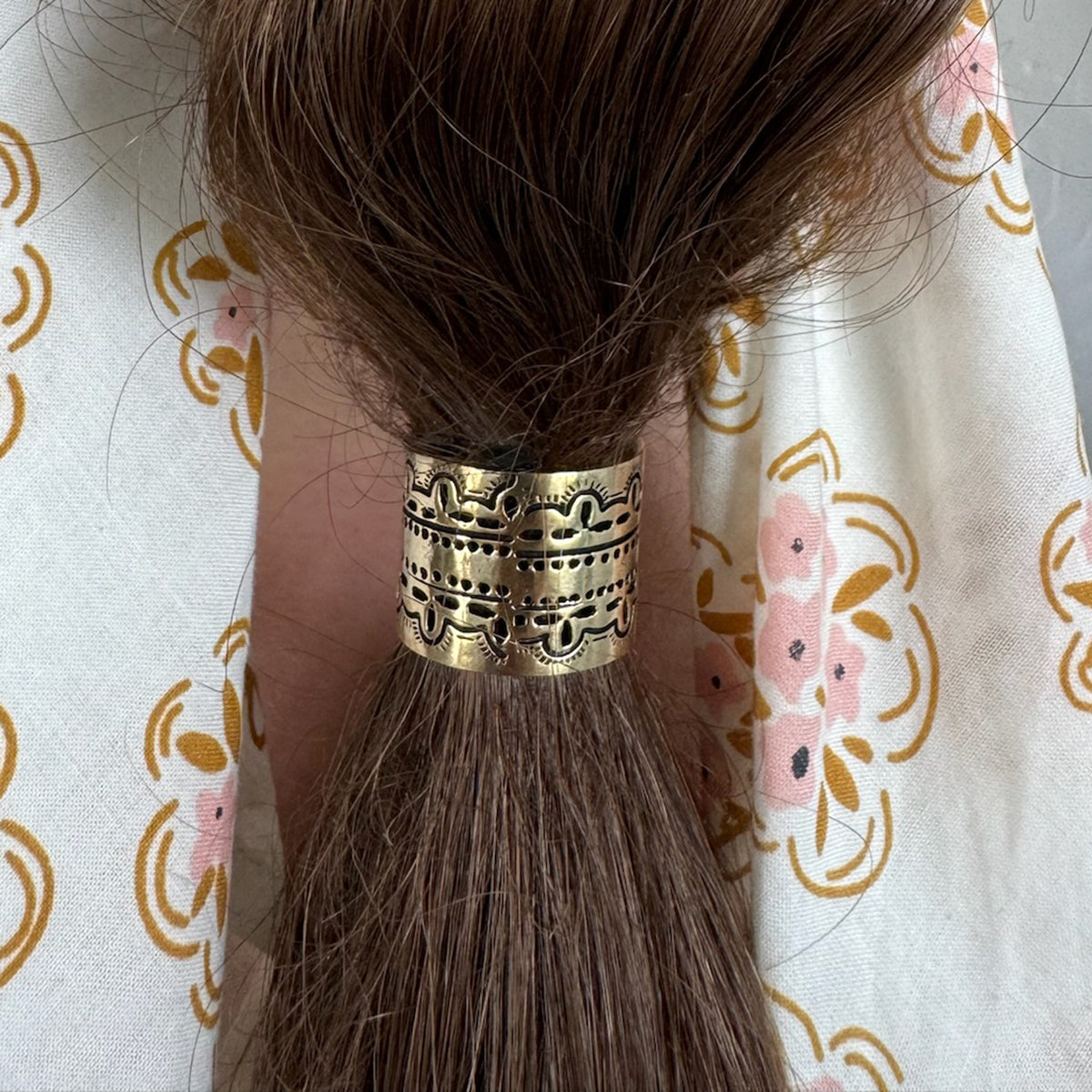 Brass hair cuff on brown hair against floral fabric.