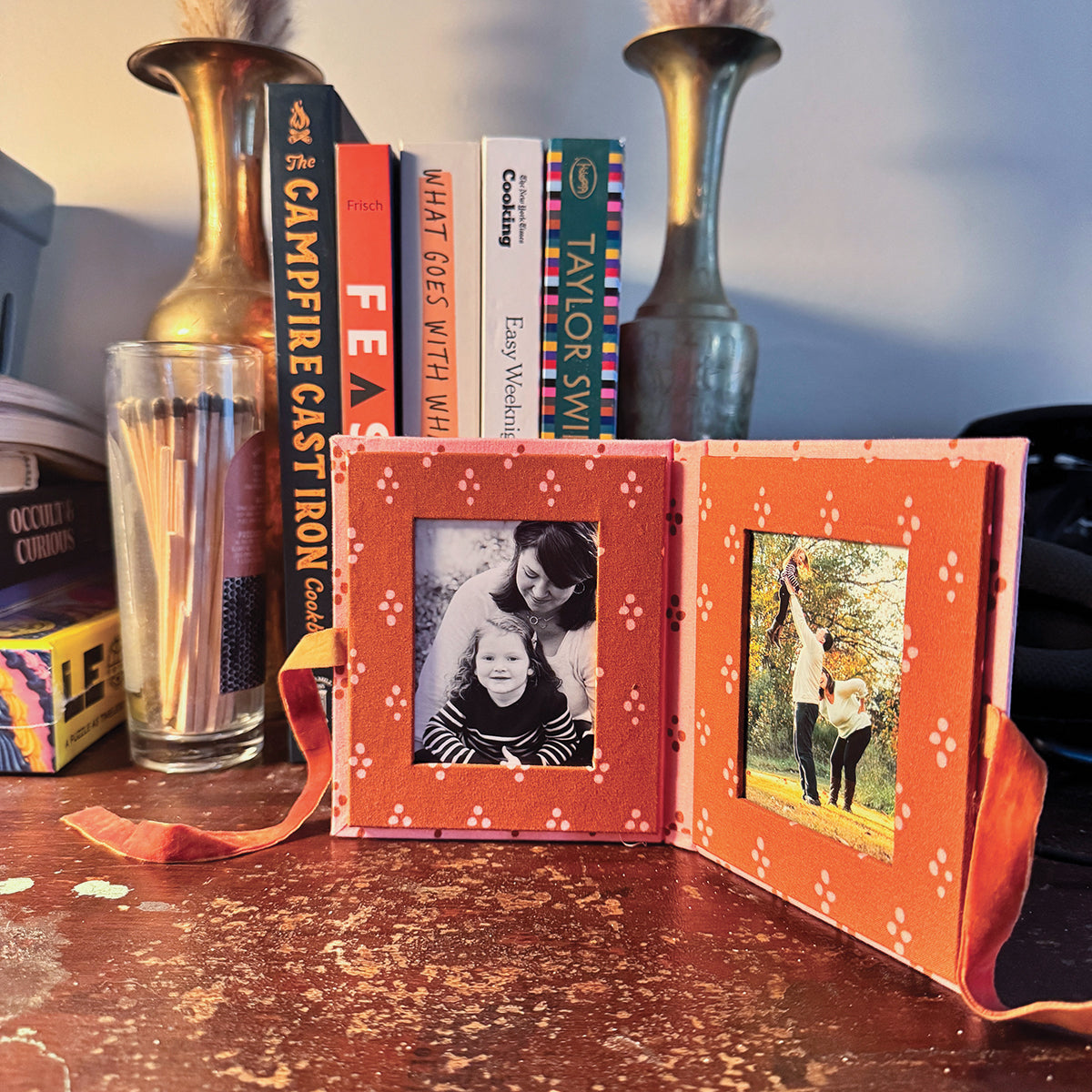Open orange mini photo-album on table with left black-and-white portrait of two children and right color photo of person with dog.