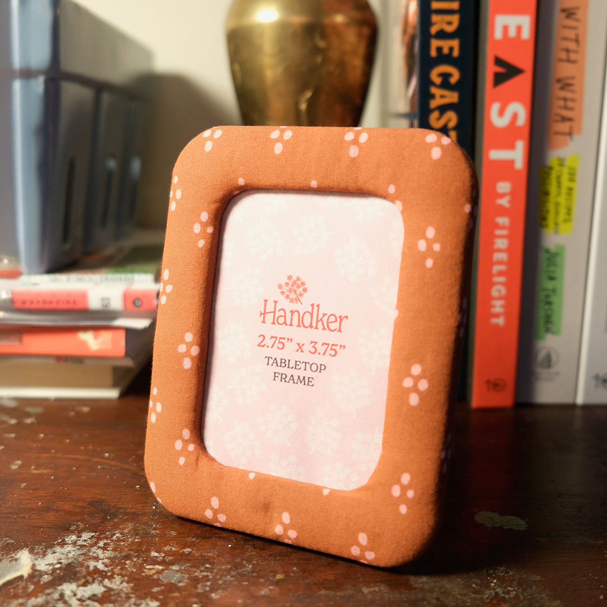 Handker fabric tabletop frame with red and pink dotted pattern, standing upright on a desk with books in the background