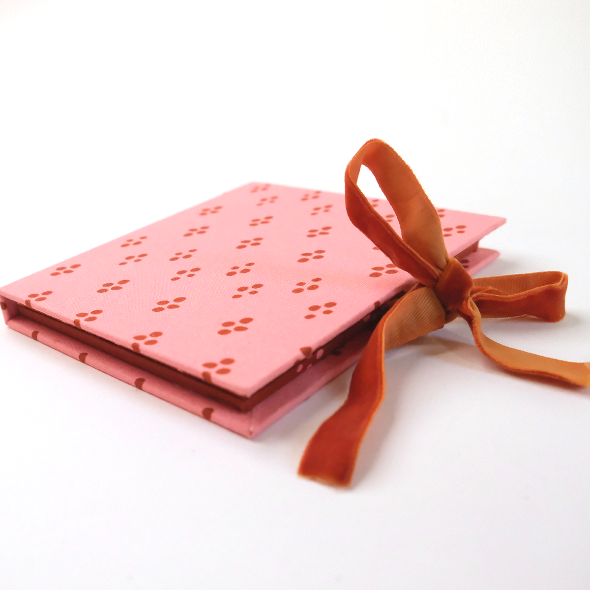 Pink hardcover journal with perforated floral pattern and orange velvet ribbon tied in a bow.