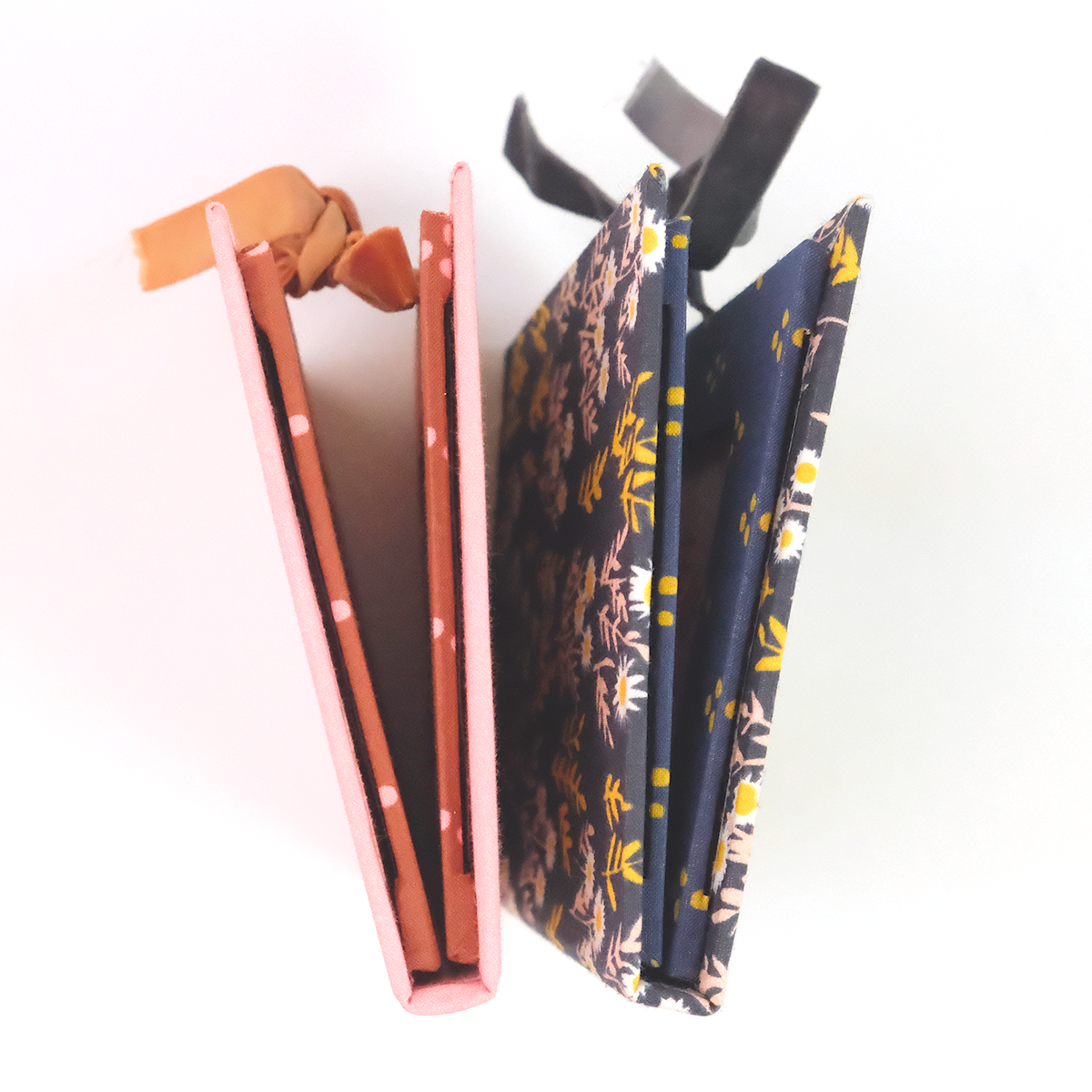 Two folded eyeglass cases side-by-side: metallic pink case and navy case with yellow floral pattern on white background.