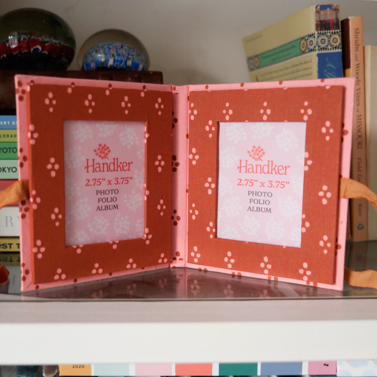 Open orange scrapbook-style display with two patterned inner pages and white centered labels on a shelf