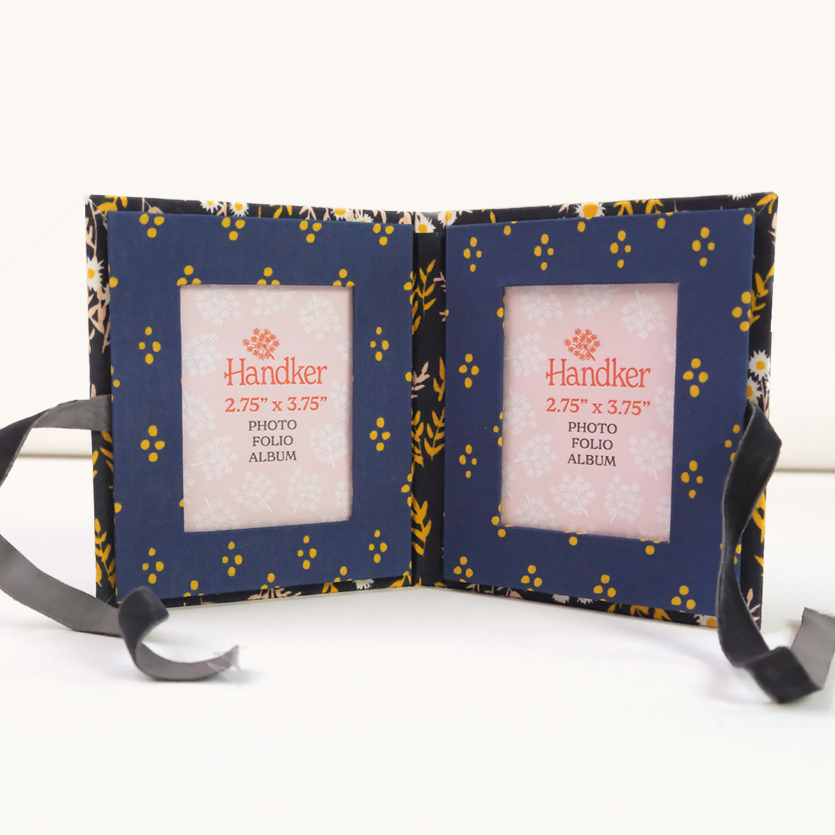 Open navy fabric sample booklet with yellow floral pattern, two centered product label cards, and tied black ribbons