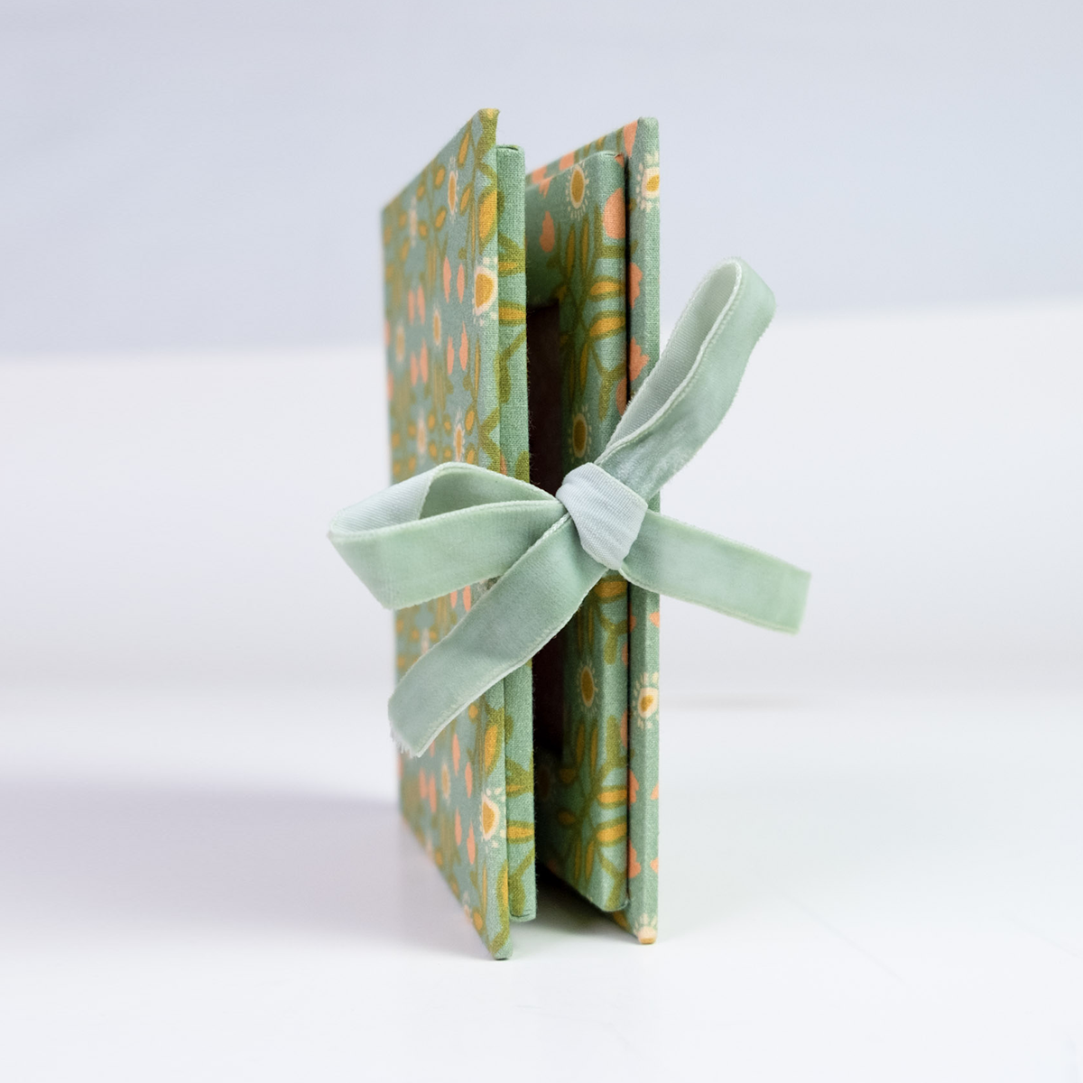 Angled view of Katie Fabric Folio Frame showing green floral fabric cover and ribbon tie closure on white background