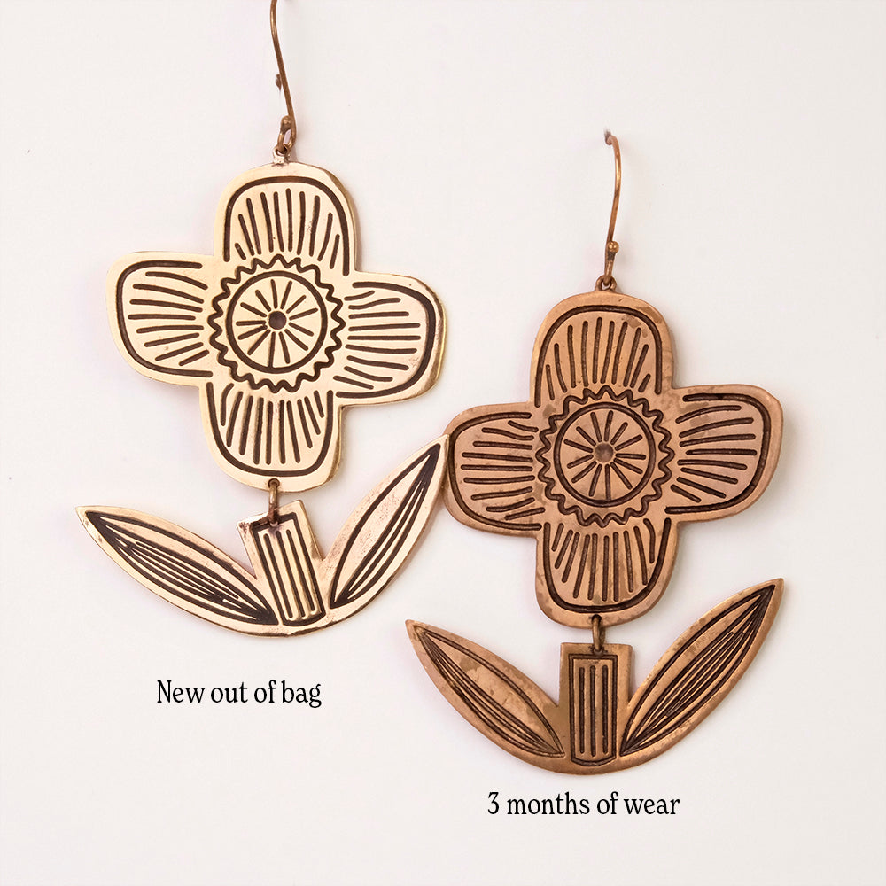 Two earrings shaped like flowers, one labeled 'New out of bag' and the other labeled '3 months of wear', showing a color difference.