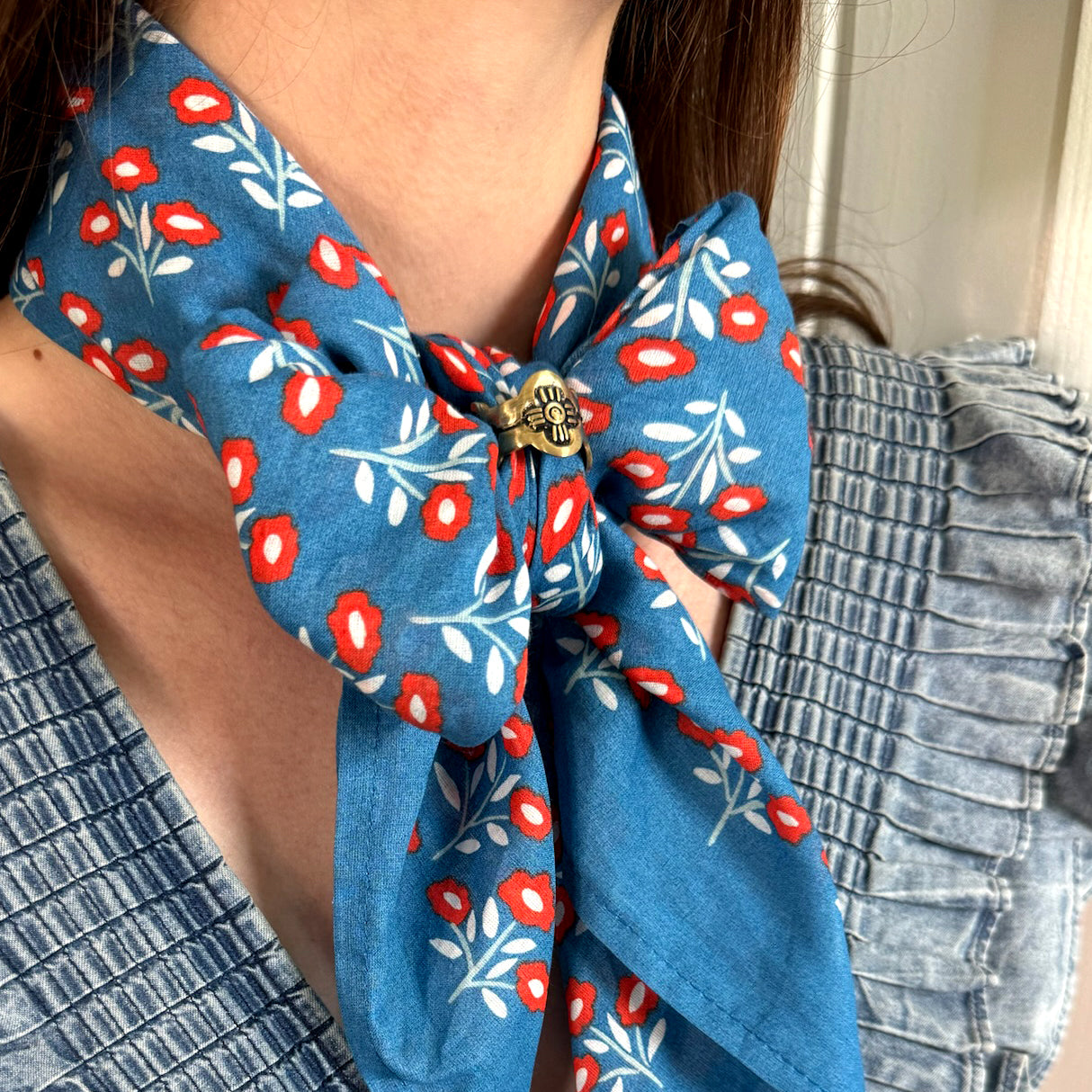 Blue scarf with small red flowers tied in a bow at the neck, secured by a small gold bee-shaped pin