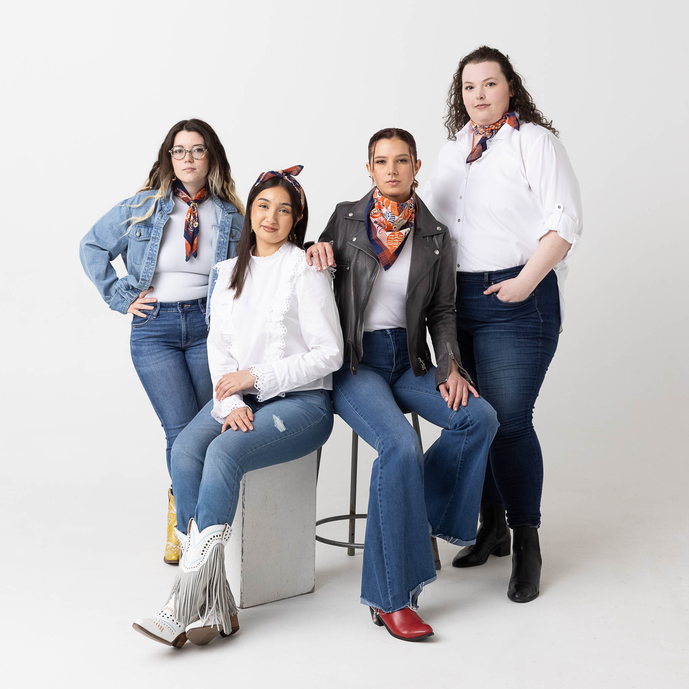 Four adults in casual denim and white tops posing against a white background—two seated, two standing.