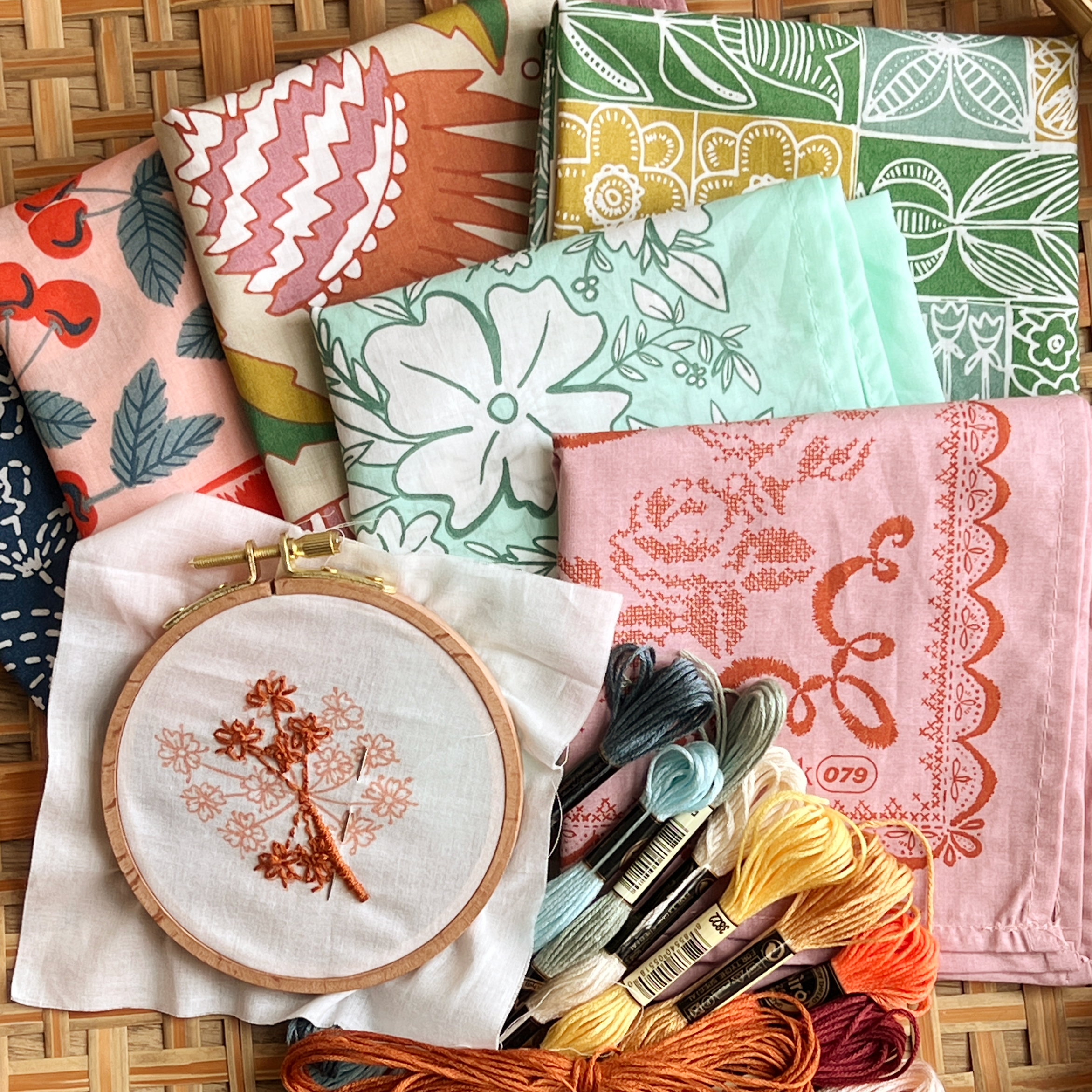 Top view of Hemlock bandana embroidery kit with embroidered floral hoop, colorful bandanas, and embroidery floss on woven mat