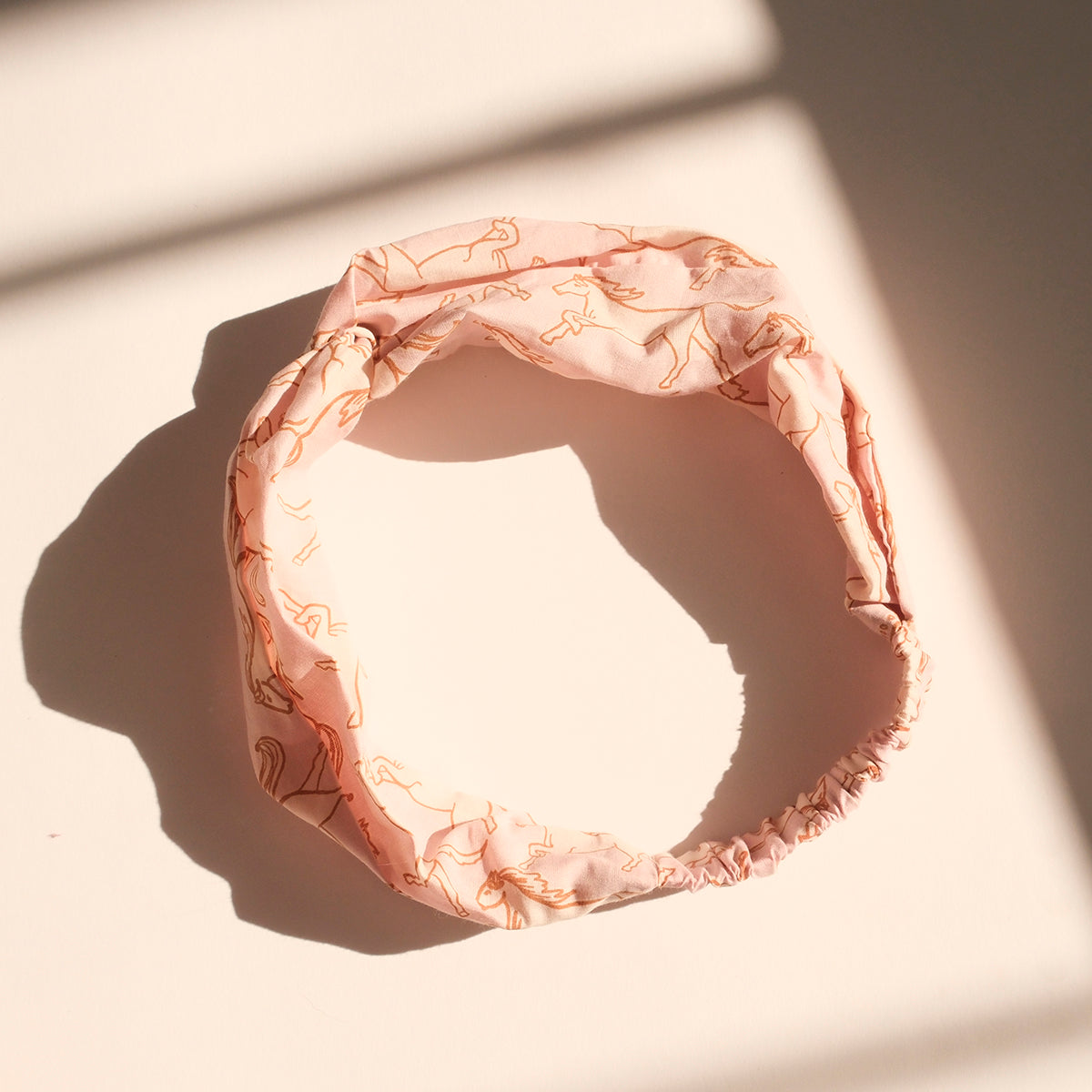 Pink fabric hair scrunchie on sunlit surface, casting a shadow.