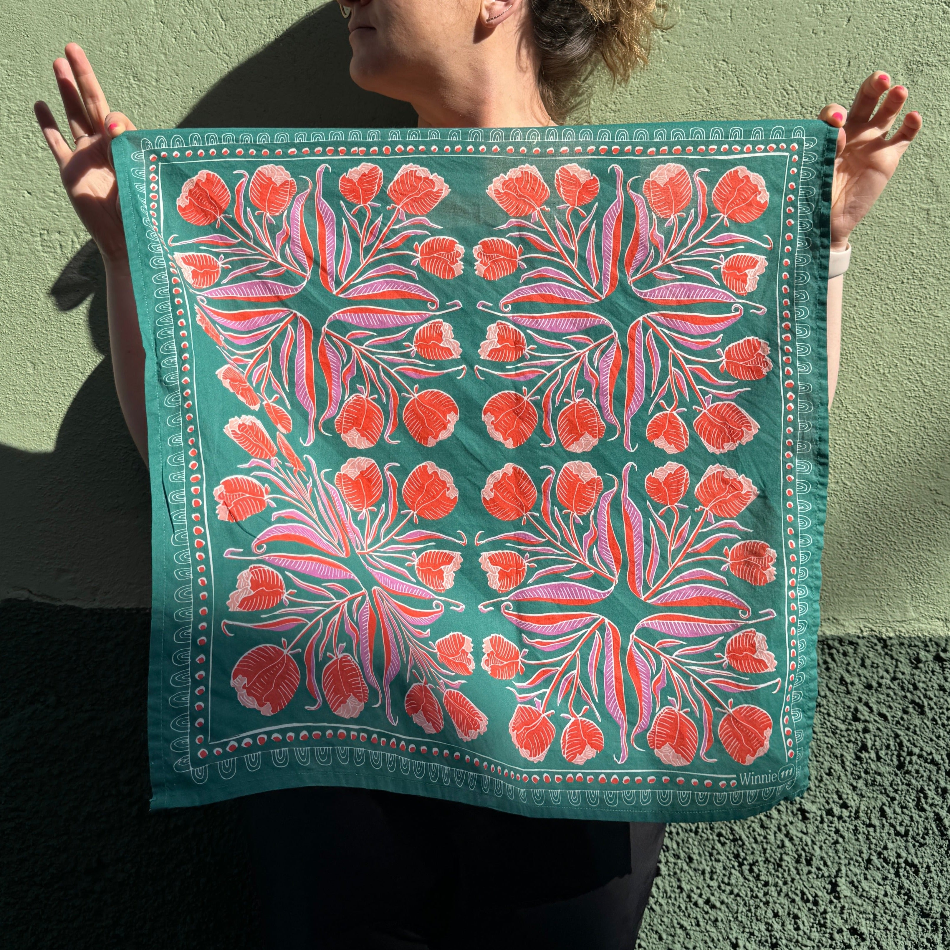 Person holding a colorful, floral patterned fabric with red flowers against a green background.
