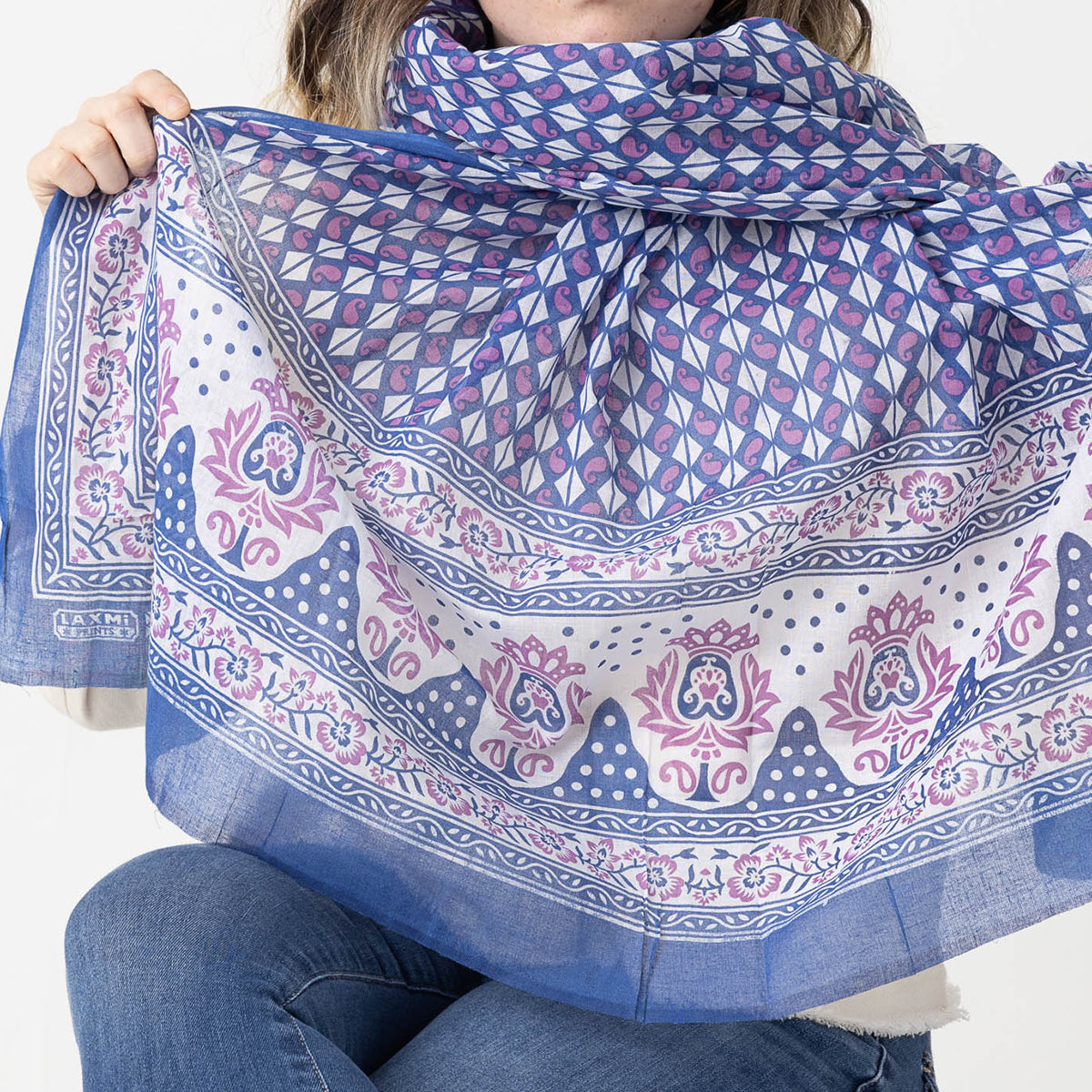 Woman holding blue and pink paisley print scarf on lightweight fabric against white background