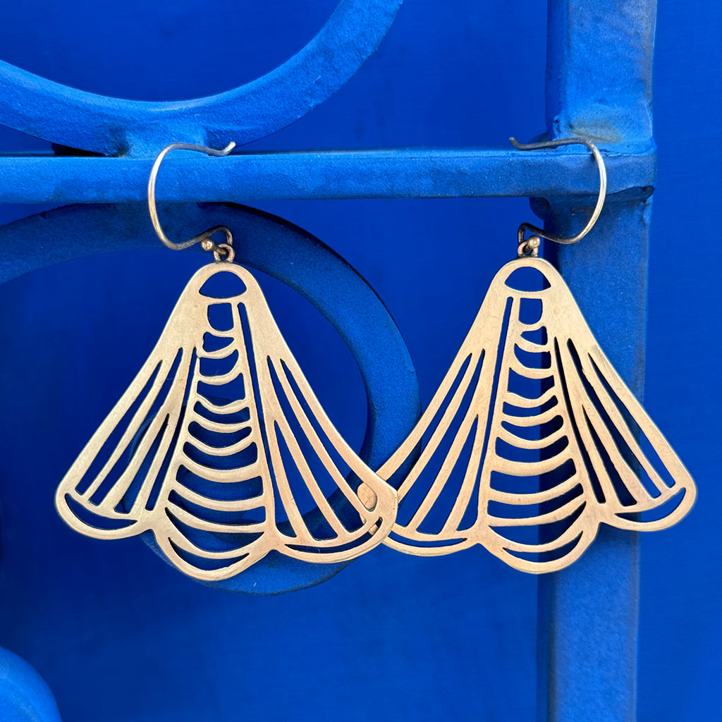 Gold geometric earrings with a fan-shaped design against a blue background.