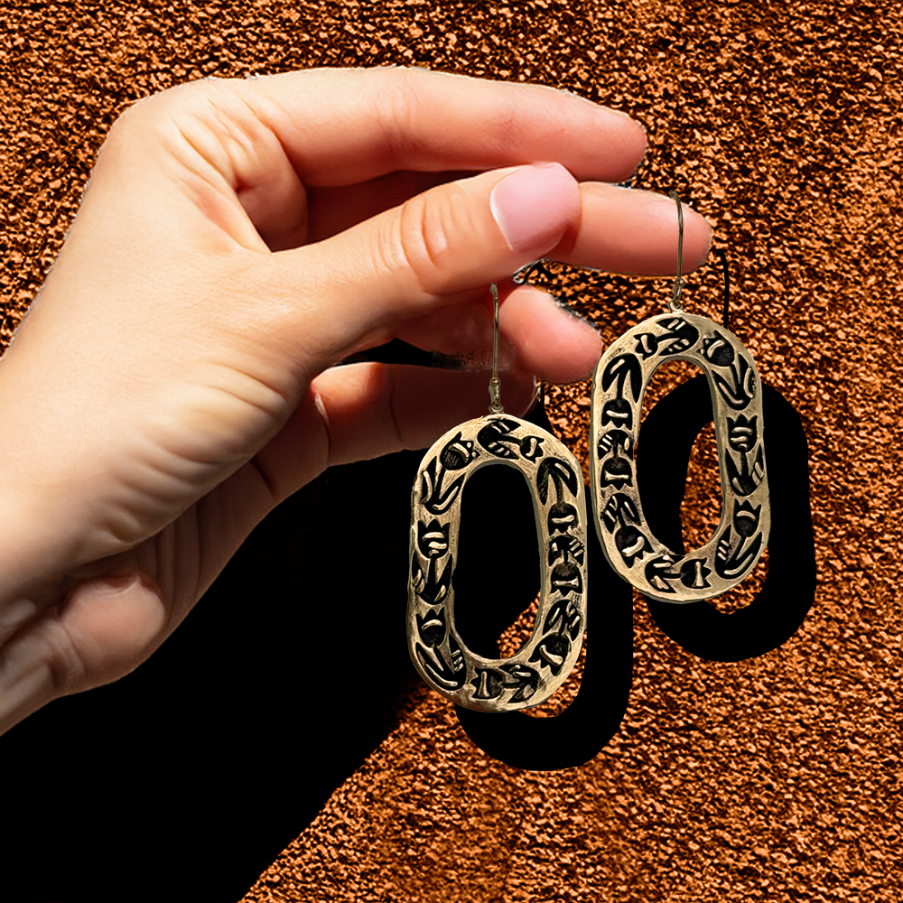 Hand holding two ornate gold earrings against a textured background.