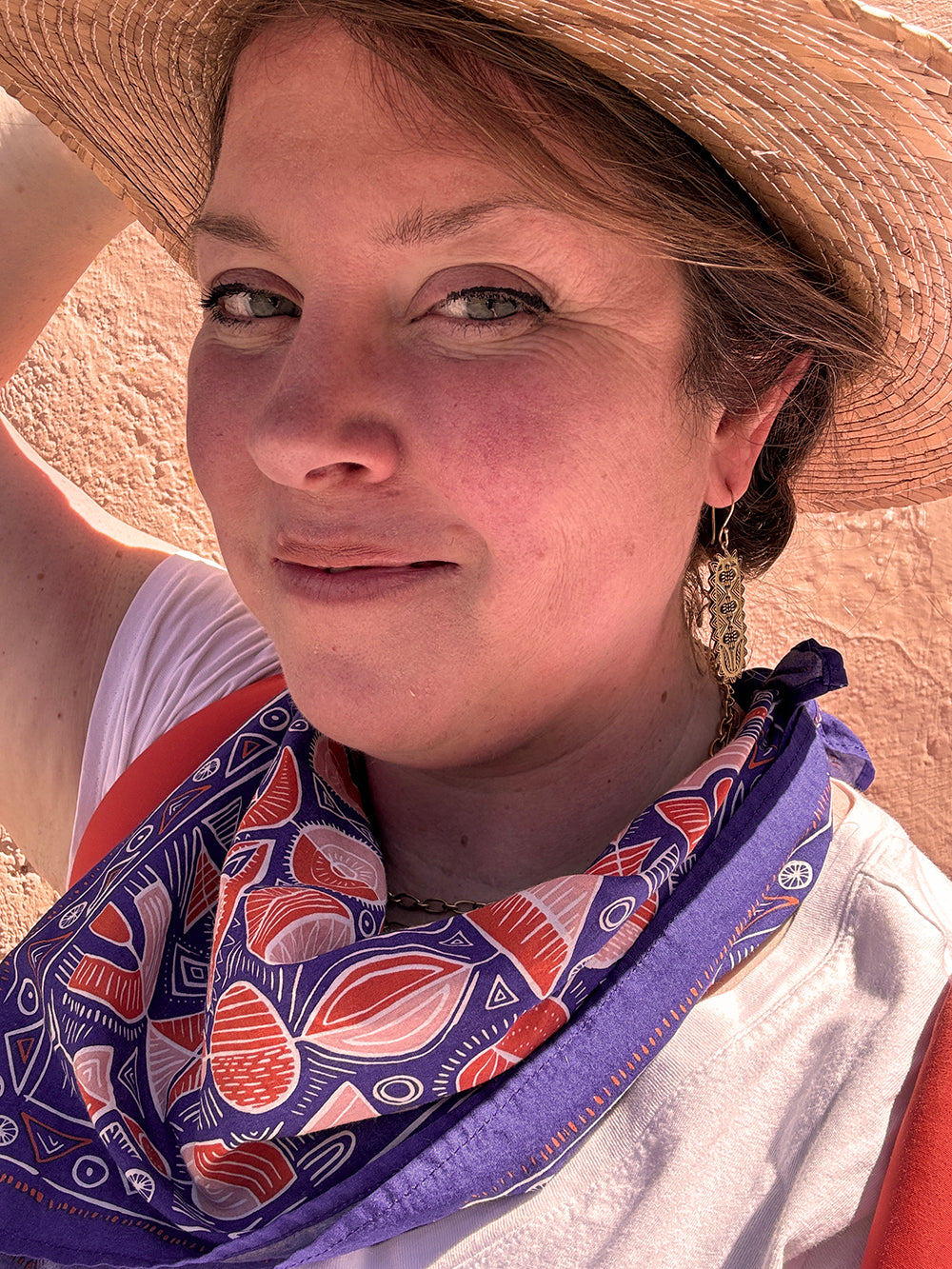 Woman wearing a straw hat and patterned scarf smiles at the camera.