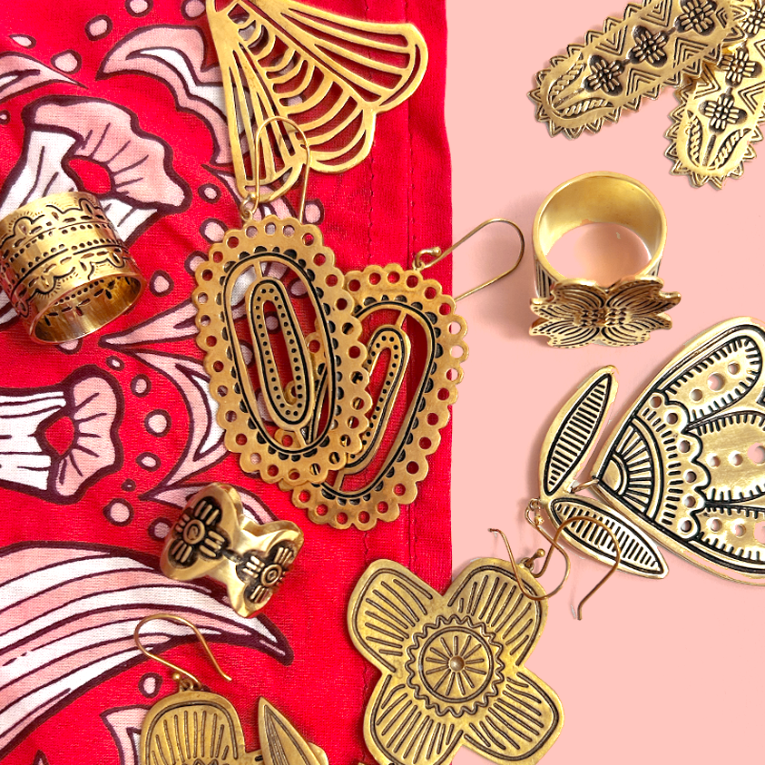 Flat lay of gold-tone earrings and rings with filigree cutouts and engraved details on red bandana and pink background