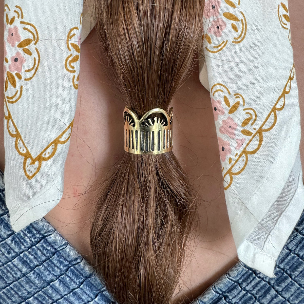 Close-up of a person with long brown hair tied in a ponytail using a decorative hair accessory.