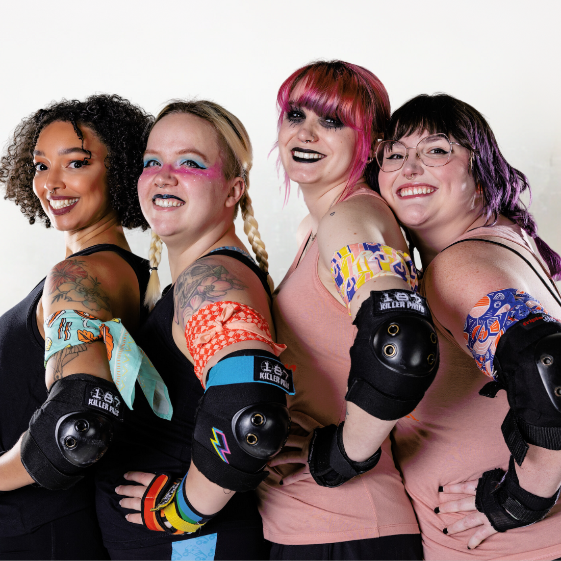 Four smiling women in roller derby gear standing together.