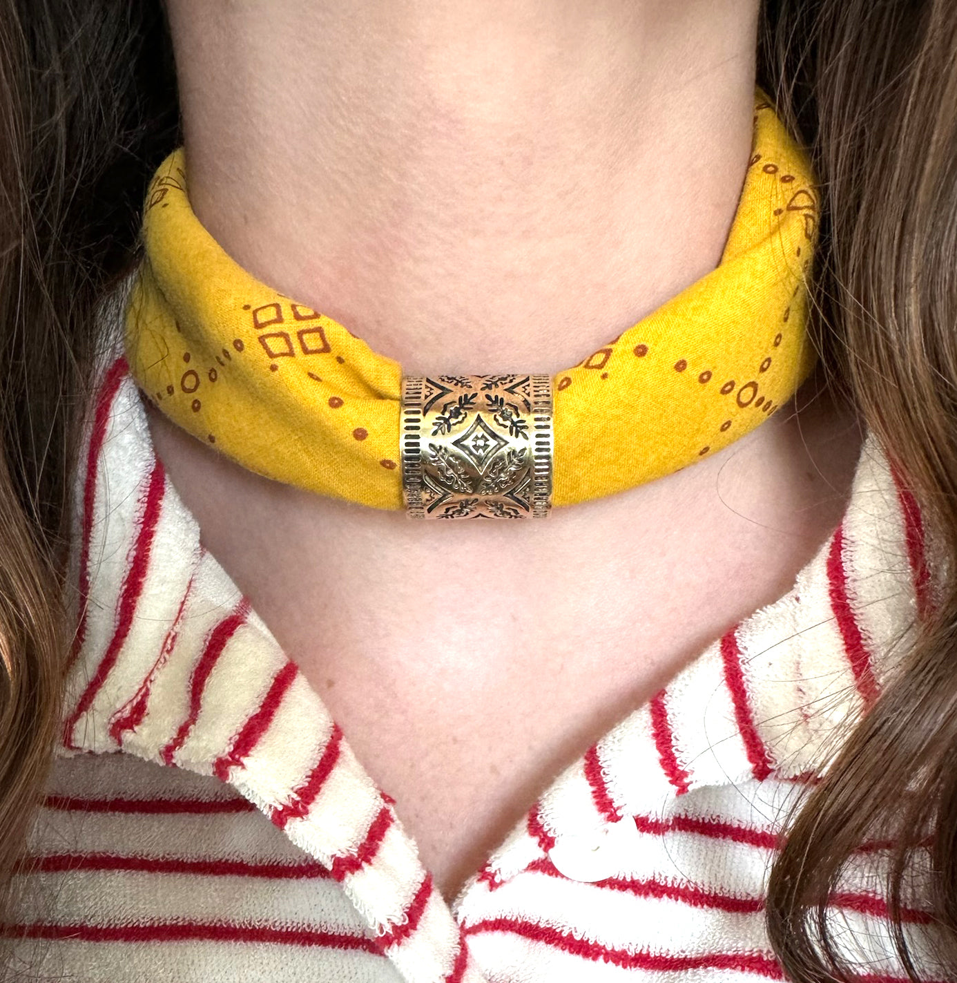 Person wearing a yellow bandana choker with a silver decorative piece.