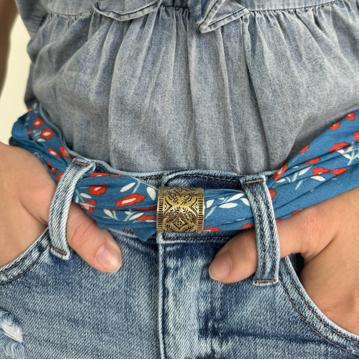 Person wearing denim jeans with a decorative belt and hands in pockets.