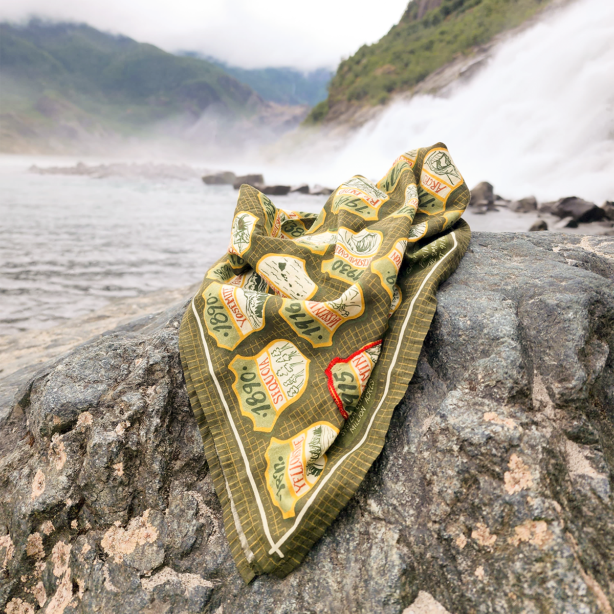 Green patterned green national parks bandana with patches on a rock by a misty mountain lake