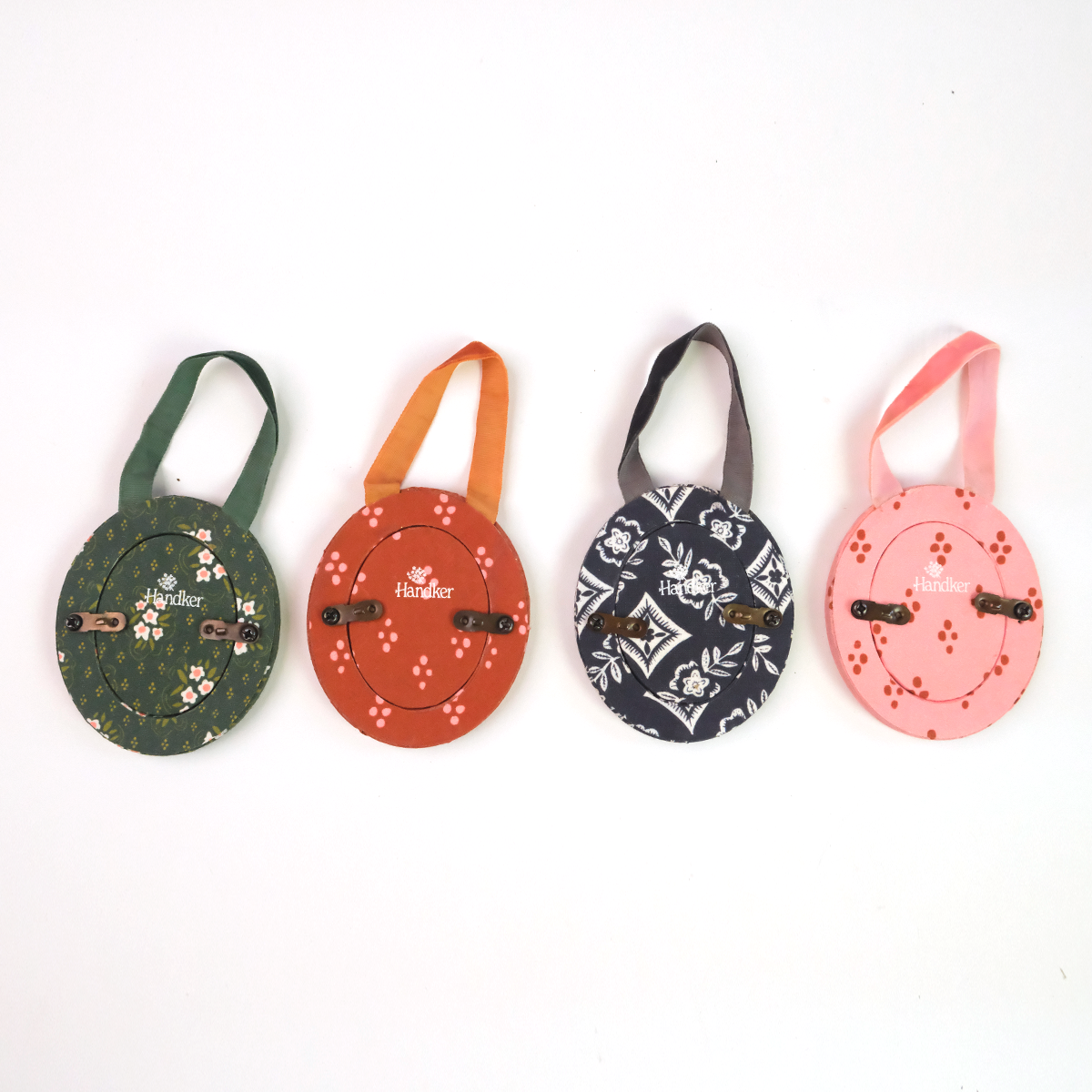 Four round zip coin purses with short wrist straps in green, orange, navy, and pink, each with small printed motifs.