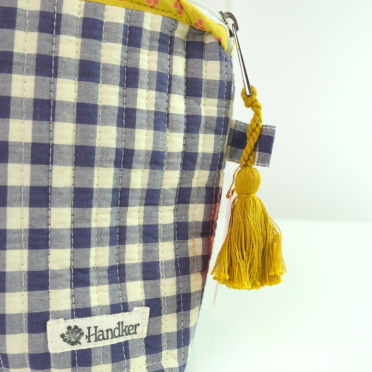 Blue and white checkered pouch with yellow tassel and 'Handker' label on a white background