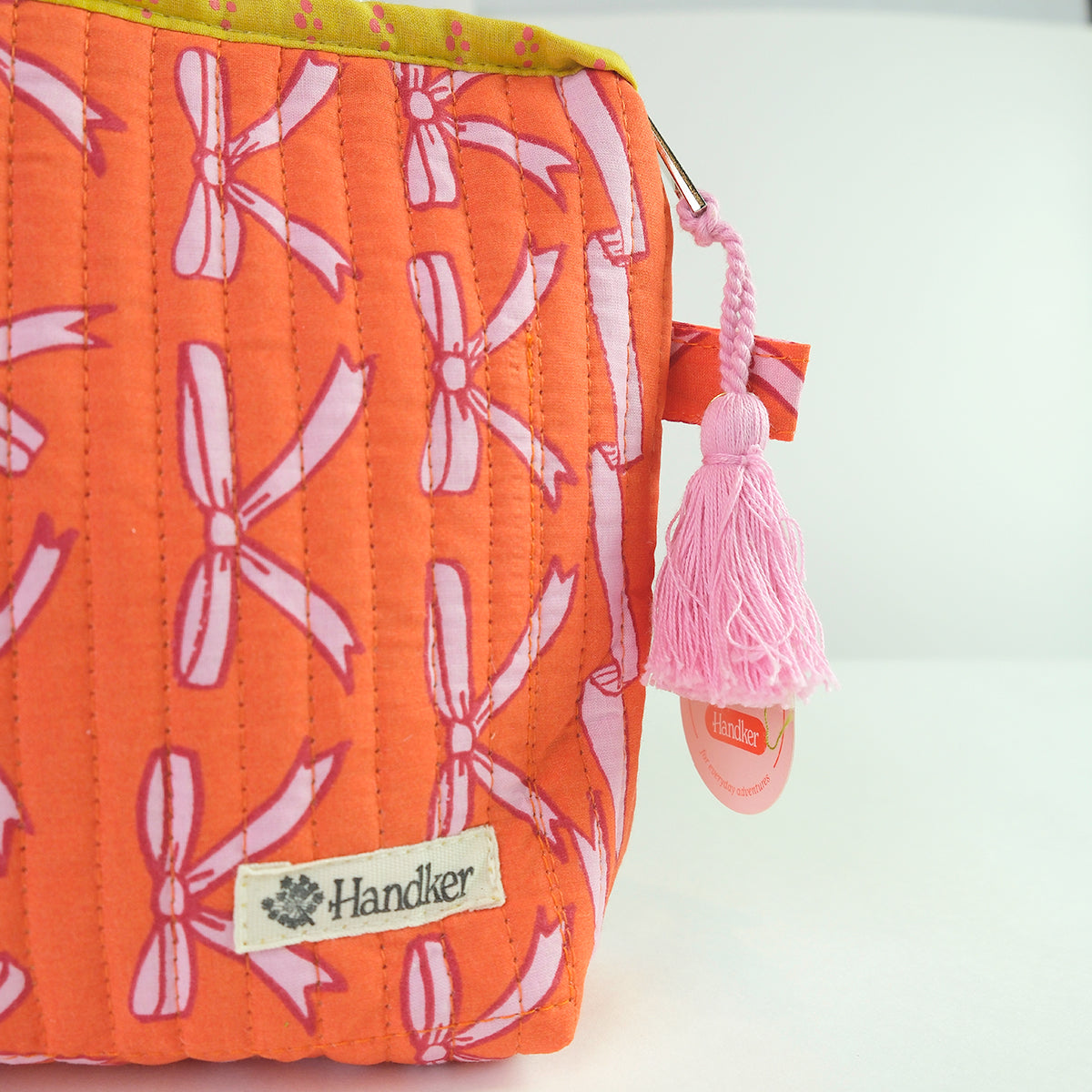 Orange pouch with pink bow pattern and tassel, featuring a 'Handker' brand label.
