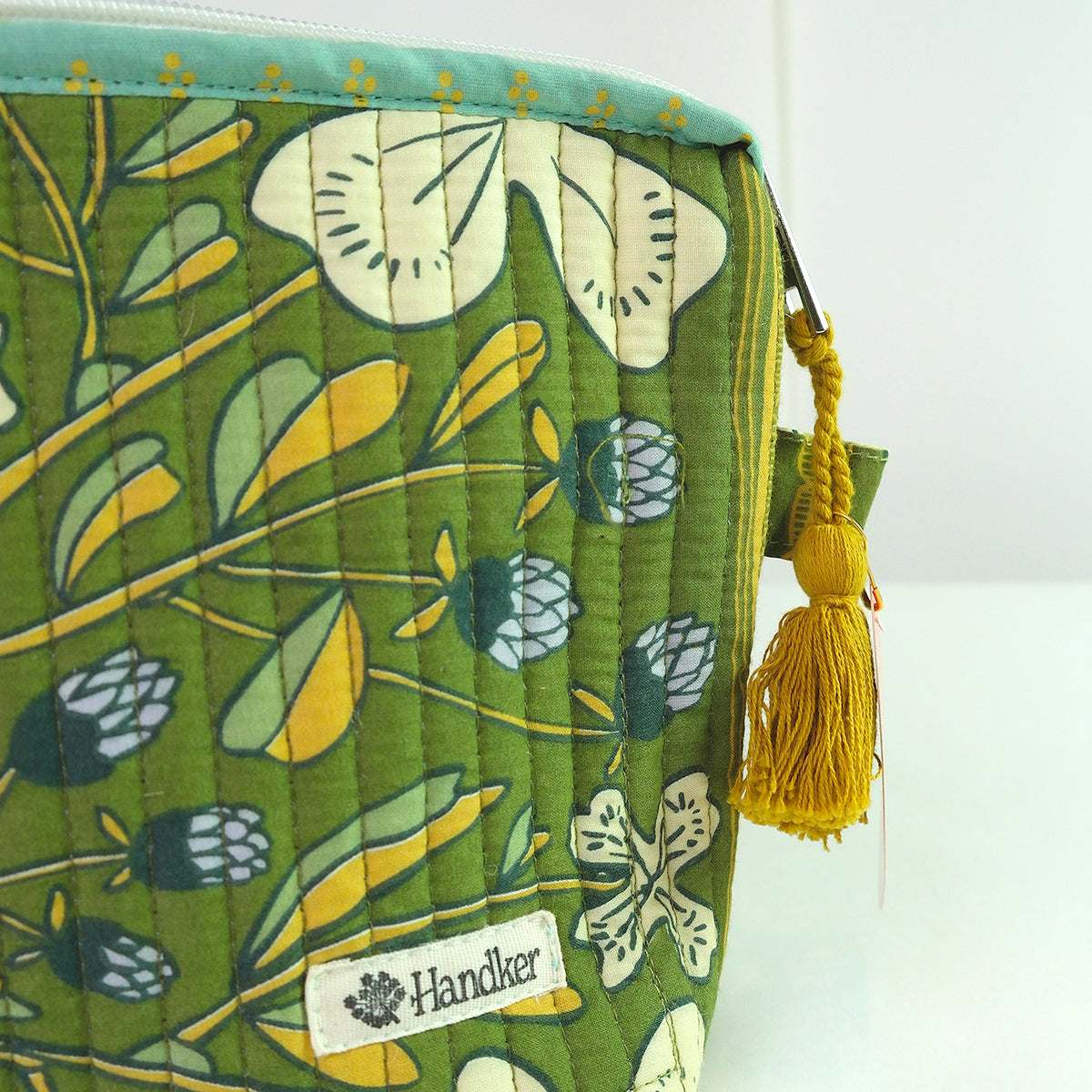 Green floral-patterned bag with a yellow tassel and 'Handker' label on a white background
