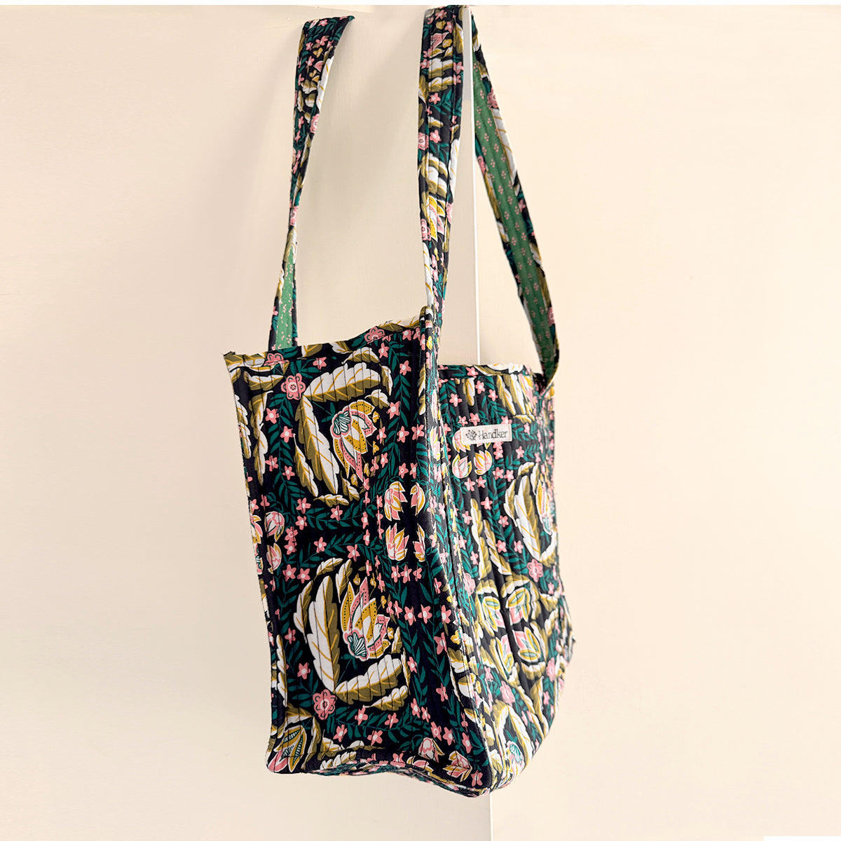 Quilted fabric shoulder bag with navy floral and paisley pattern and long narrow straps.