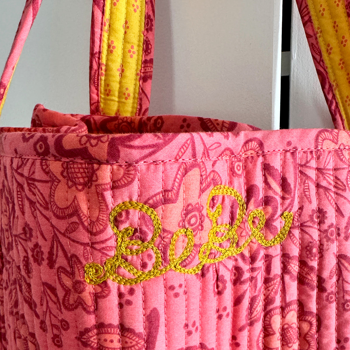 Pink quilted fabric tote bag with yellow embroidered "bebe" and matching handles