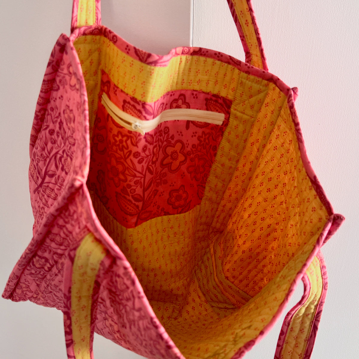 Top-down view inside quilted pink-and-orange fabric tote bag showing interior pocket and patterned lining.