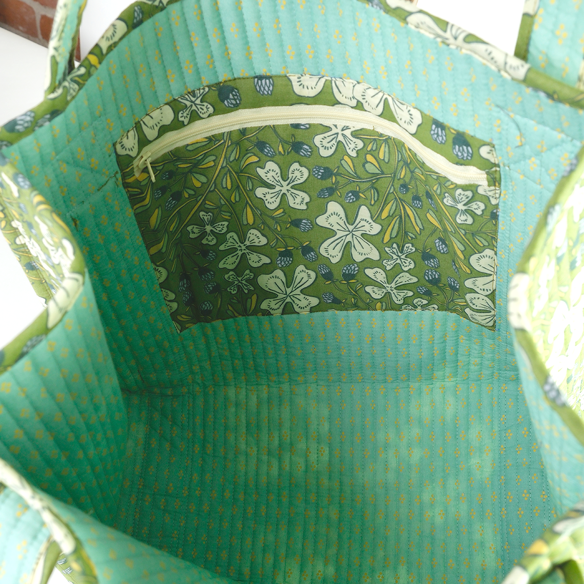 Close-up of the inside of a green fabric bag with floral patterned pocket.