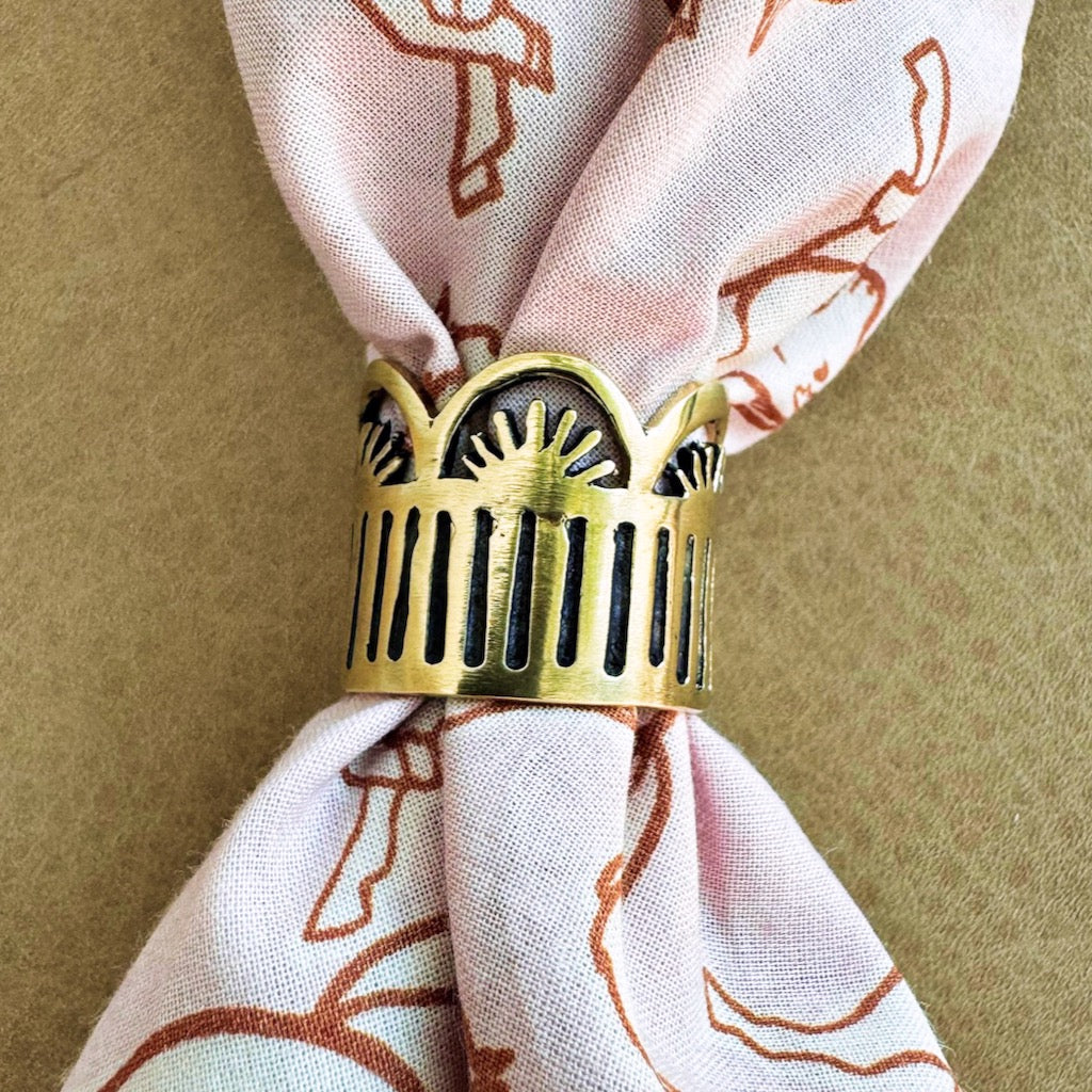 Gold napkin ring with sunburst design on a patterned cloth napkin