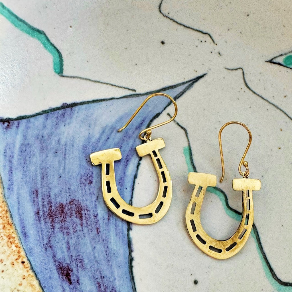 Pair of gold geometric earrings on a colorful ceramic background.