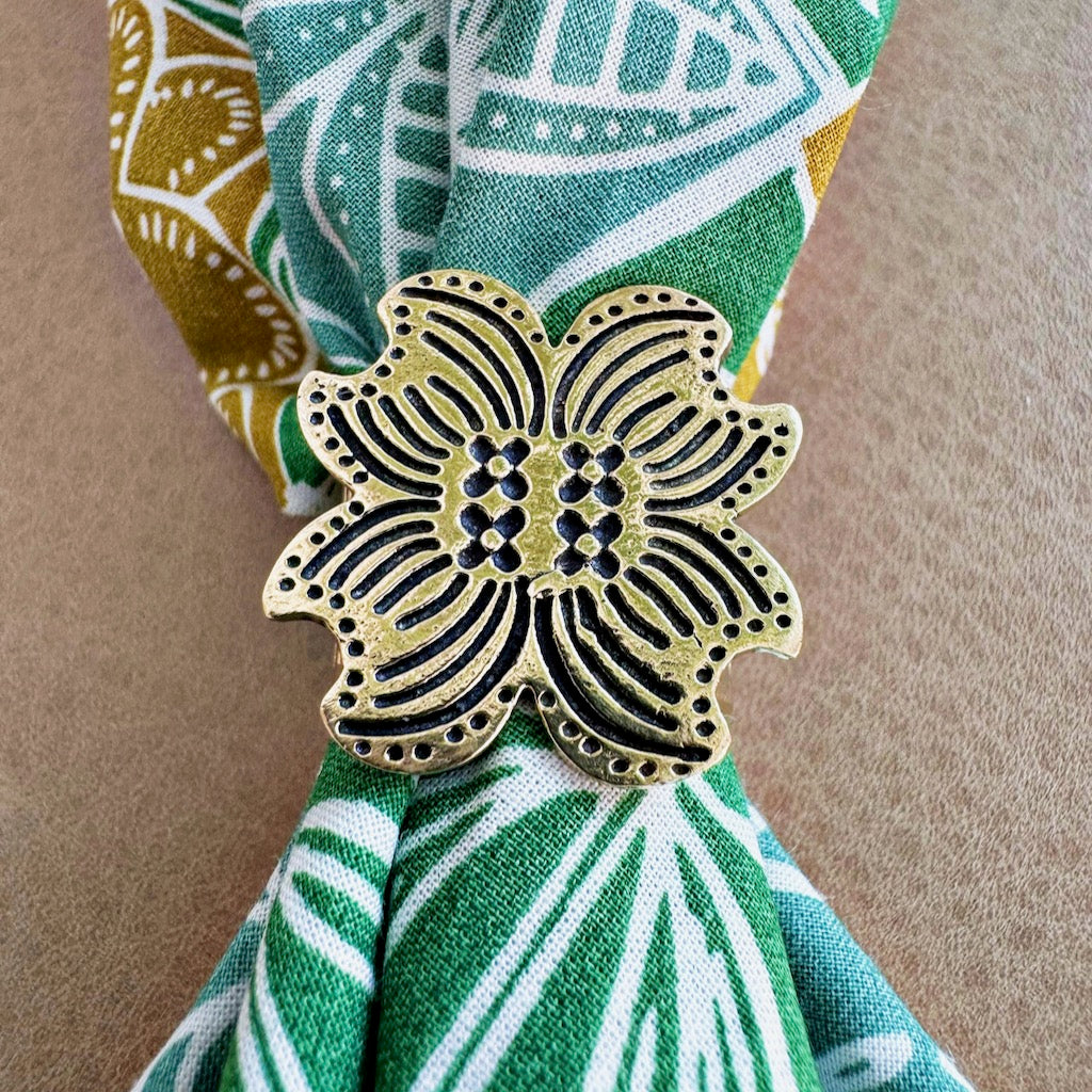 Carved wooden flower-shaped scarf ring with black dotted pattern holding green and white printed fabric