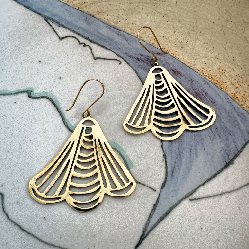 Gold fan-shaped earrings on a textured surface