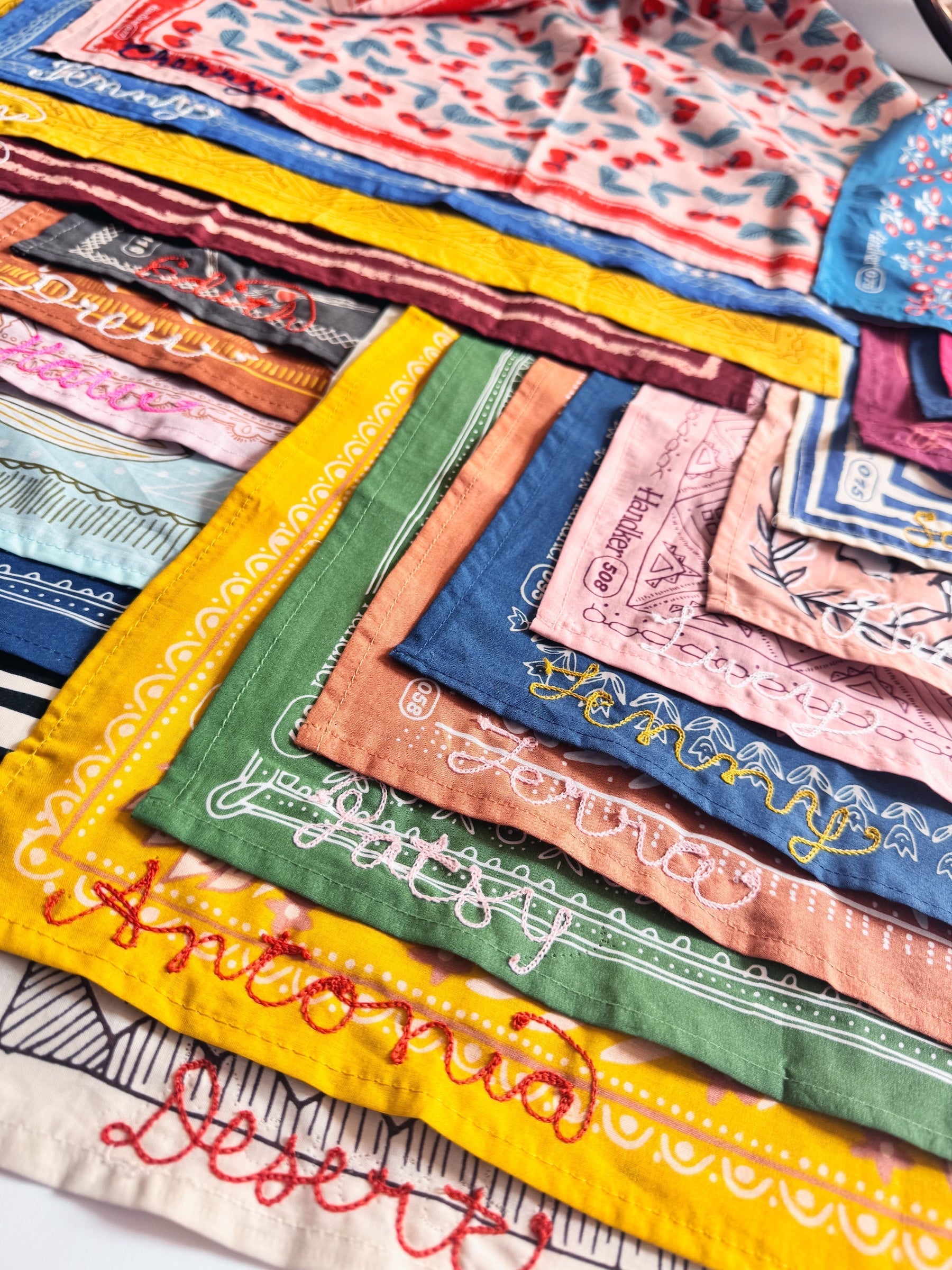 Angled close-up of Flora bandana with peach, burgundy, and green florals and stitched personalization, layered with bandanas