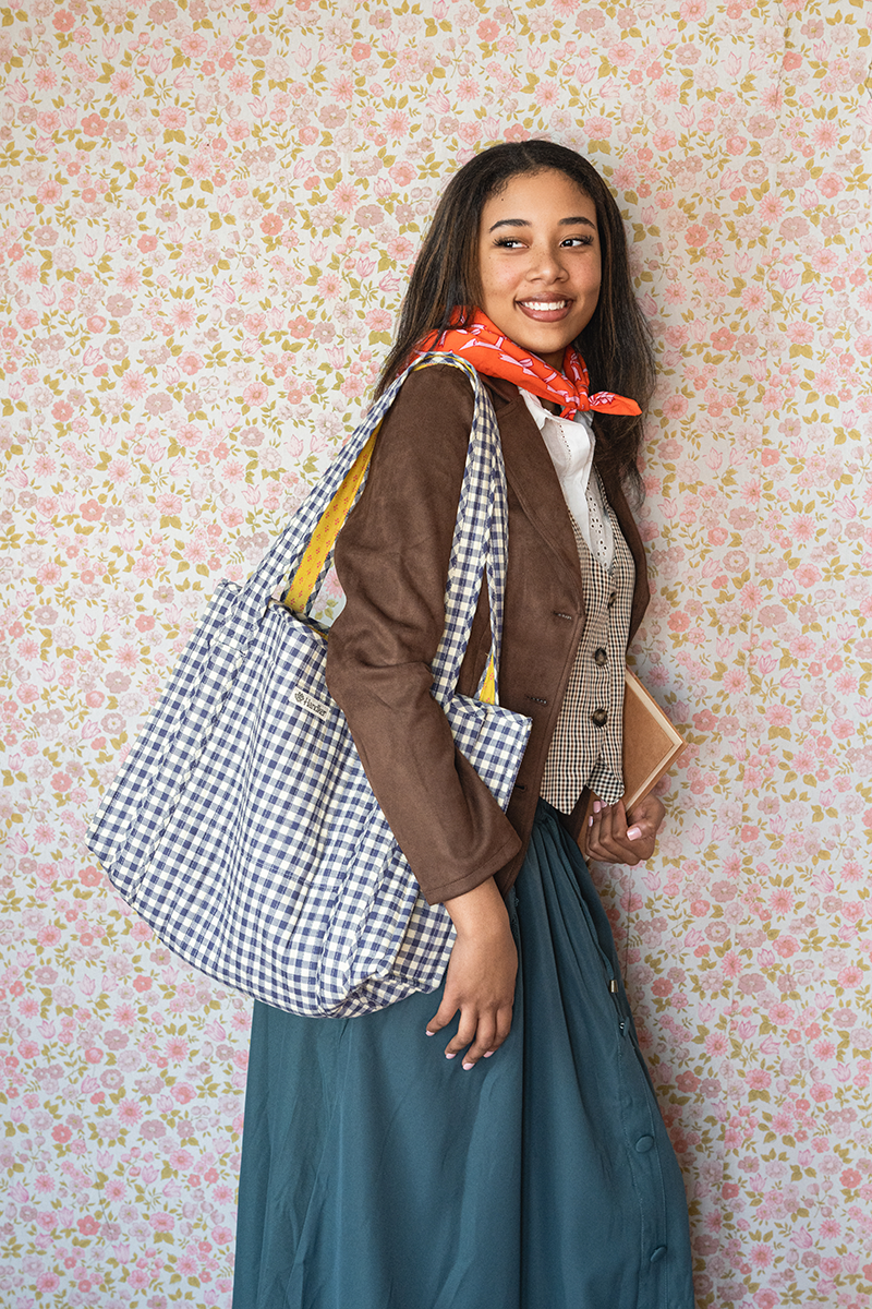 Side view of Teddy Quilted Tote showing navy and cream checkered quilting and wide shoulder straps against floral wallpaper