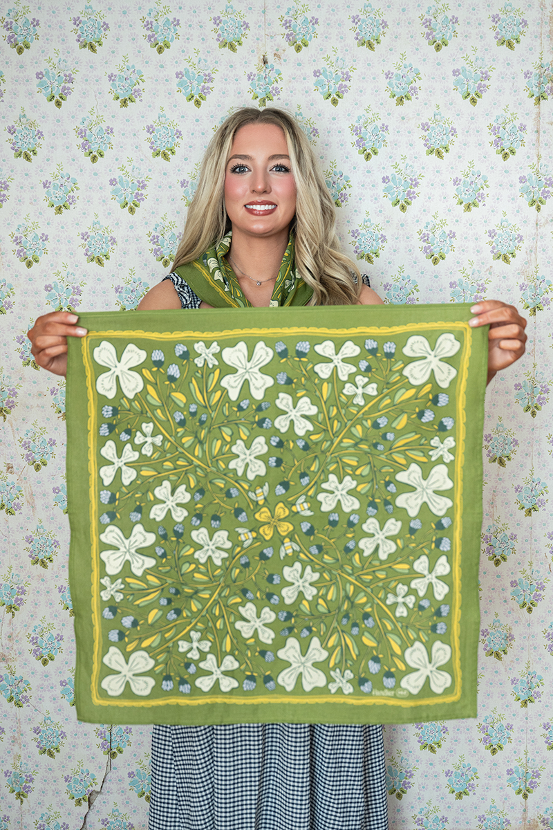 Woman holding a floral patterned green bandana against a floral wallpaper background