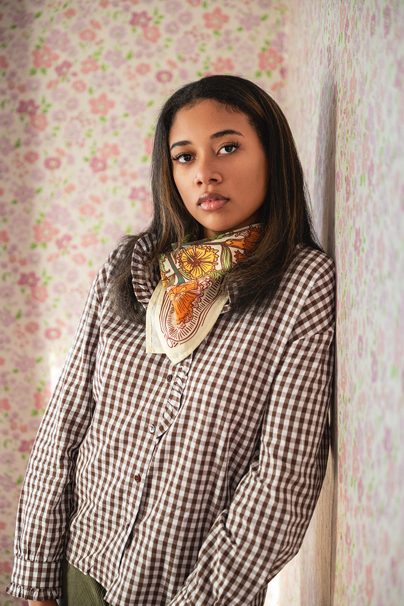 Three-quarter view of No. 153 Hannah Bandana showing cream base with orange and green floral print tied at the neck against pink floral wallpaper