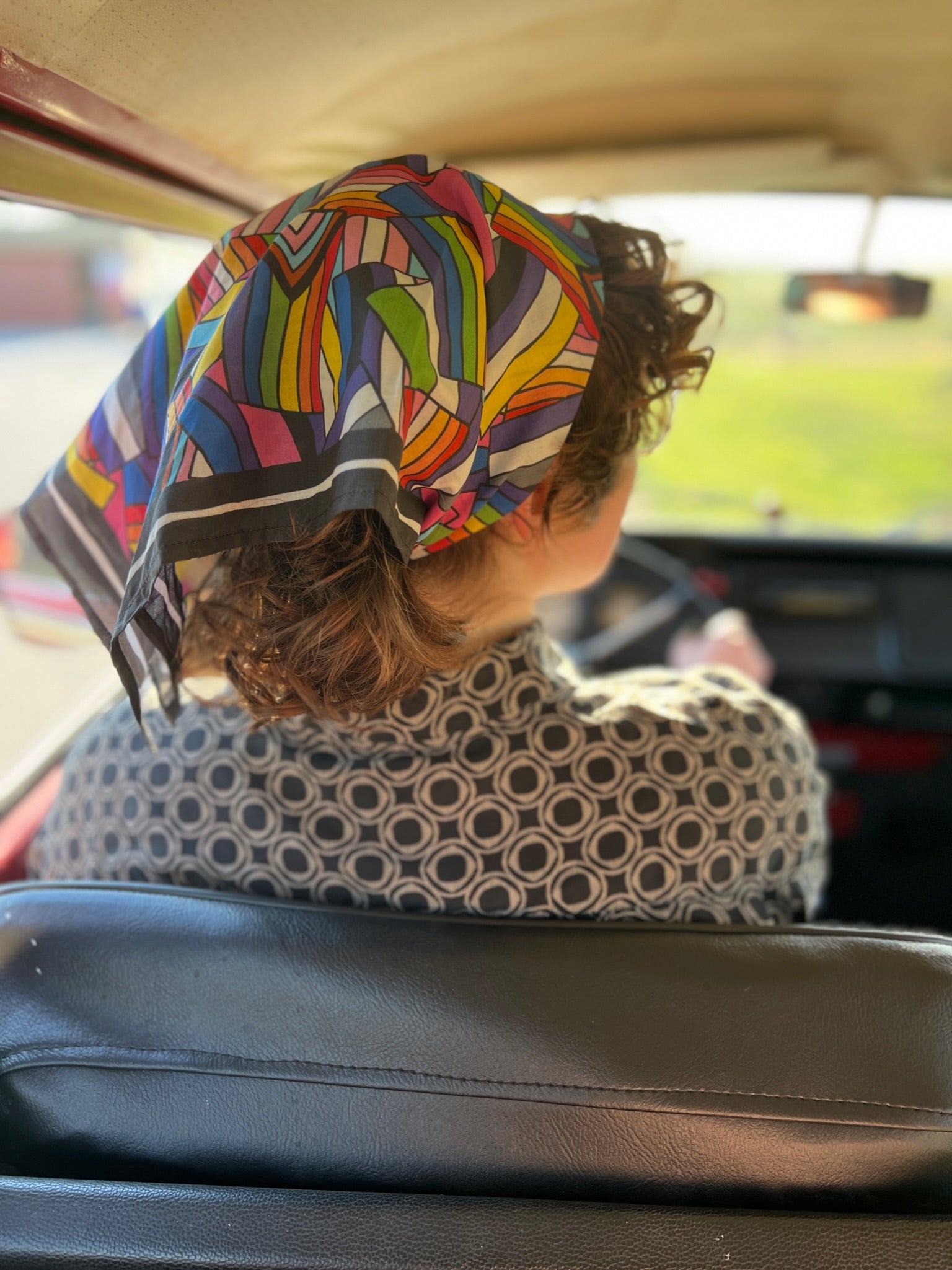 Person with colorful headscarf driving a vehicle, view from backseat